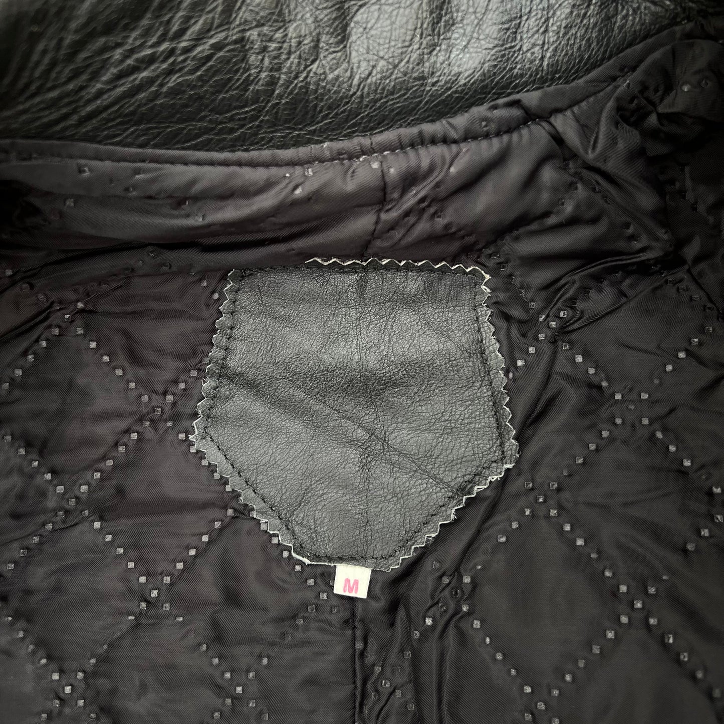 Close-up of a black quilted jacket or puffer coat showing the interior lining, diamond-stitched pattern, and a small sewn label.