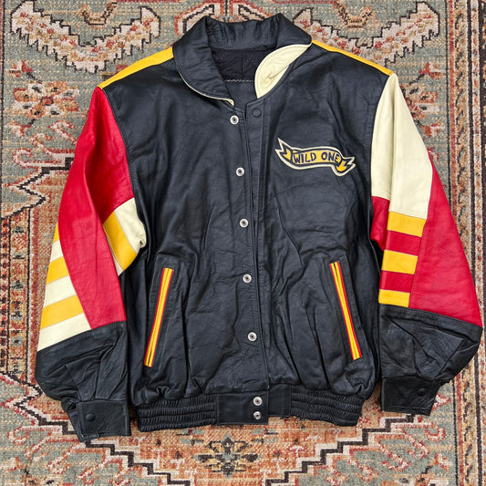 A vintage black leather varsity jacket with red and cream color-blocked sleeves, featuring a 'MILD ONE' logo patch on the left chest, laid flat on a patterned rug.