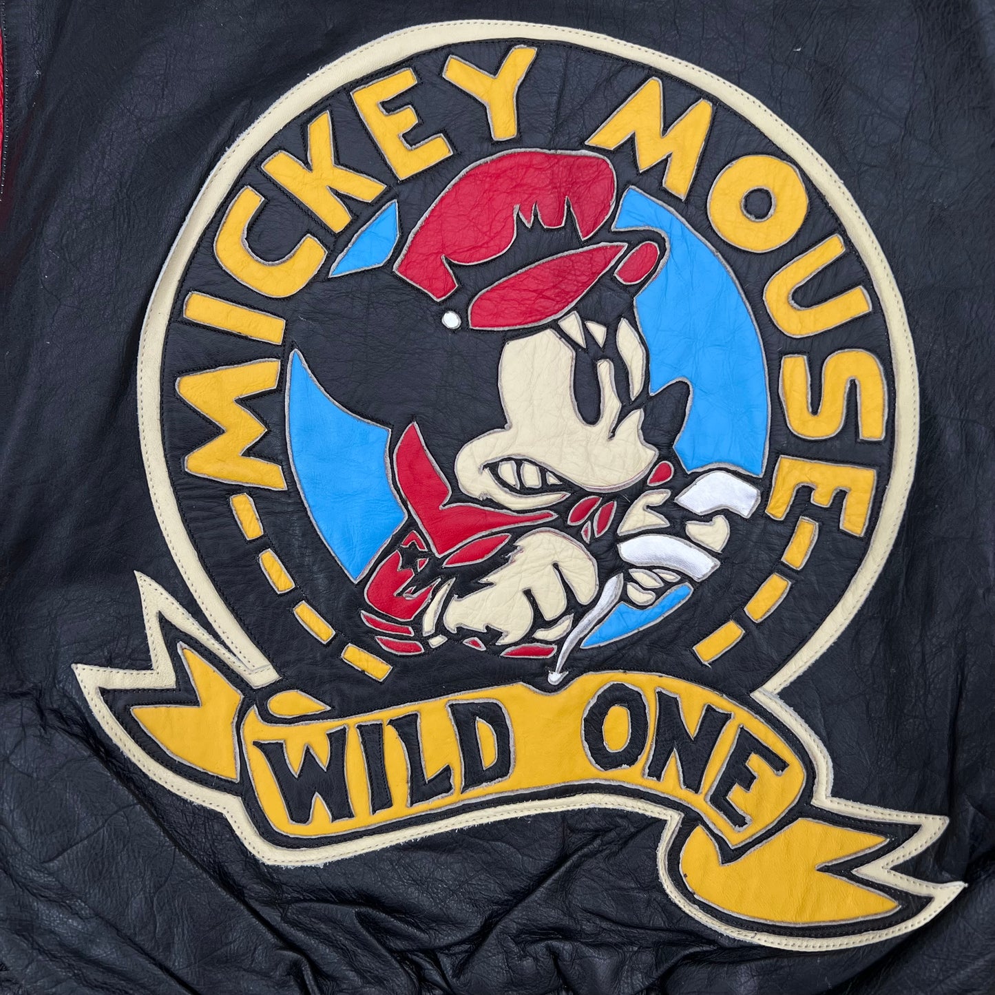 A close-up of a black fabric item featuring a large embroidered Mickey Mouse graphic with the words 'MICKEY MOUSE' and 'WILD ONE'.