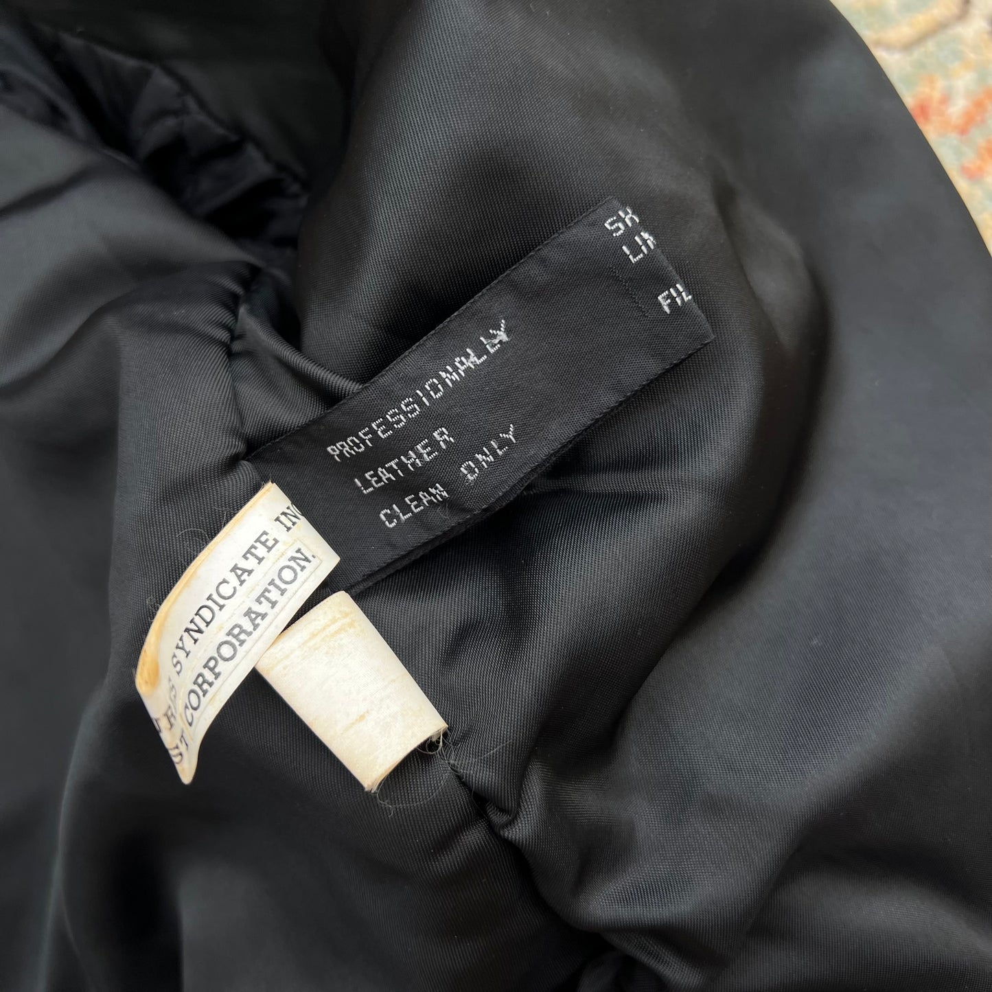 Close-up of the interior neck label of a black leather garment, showing text including 'PROFESSIONALLY LEATHER CLEAN ONLY'