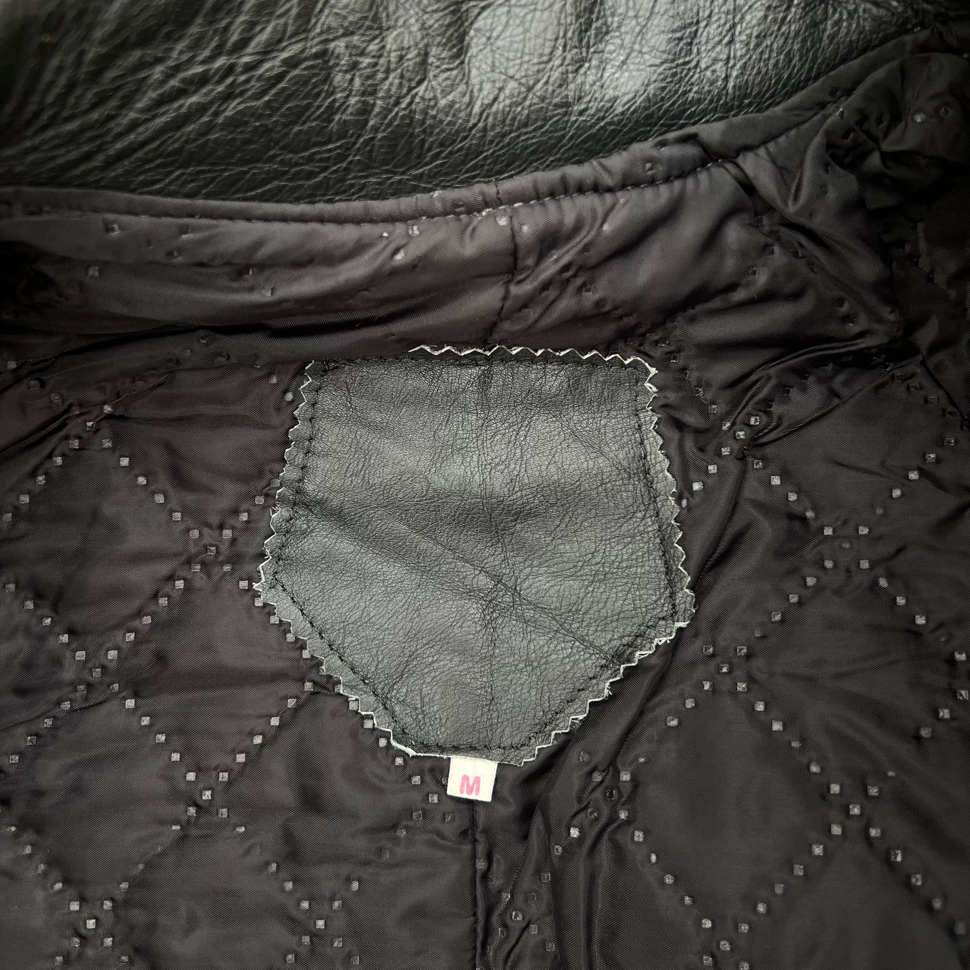 Close-up of a black quilted jacket or puffer coat showing the interior lining, diamond-stitched pattern, and a small sewn label.